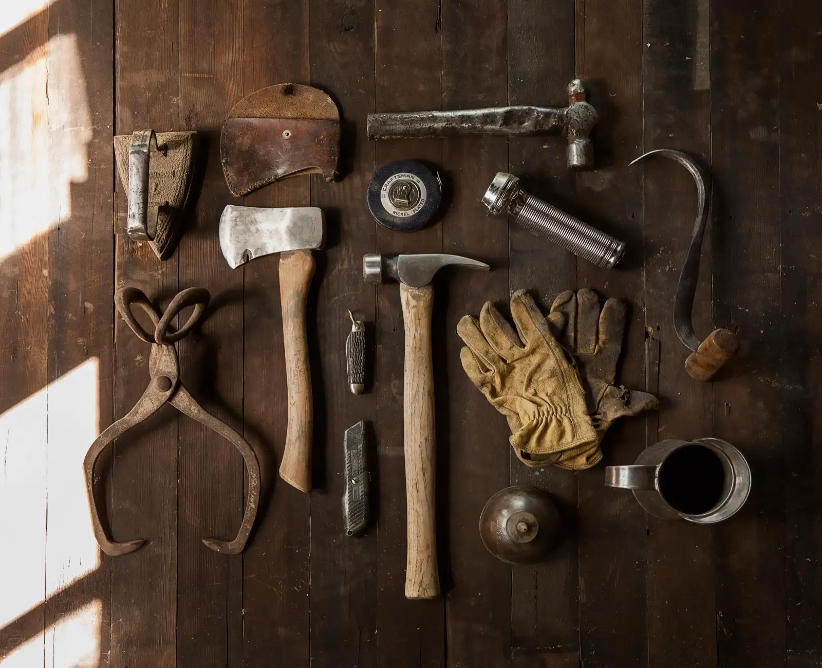 Old hand tools and leather work gloves laid out on dark floorboards